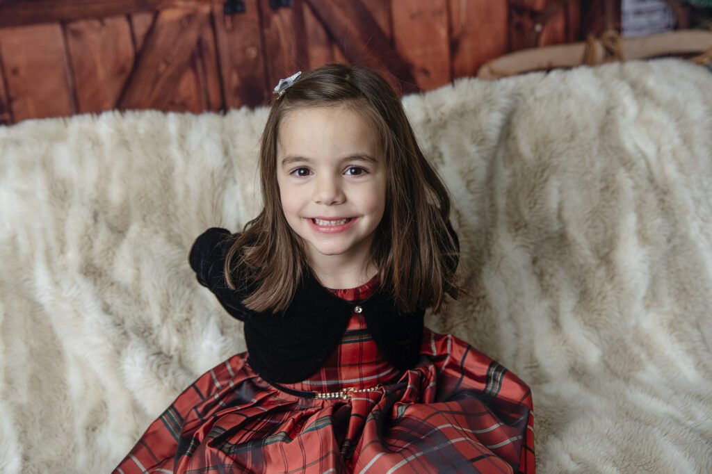 girl smiles big in beautiful holiday dress in studio holiday family photo session with Just Peachy Photography in Palatine, IL 