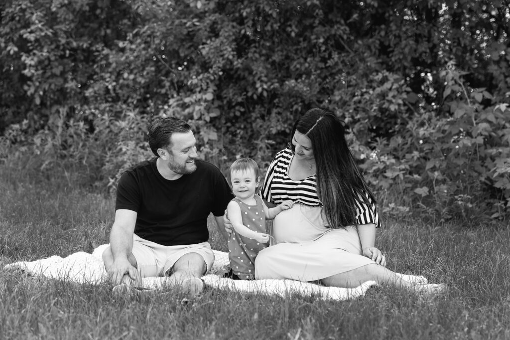maternity pictures with toddler | Mom and Dad sit together with toddler girl smiling | Photographer Just Peachy Photography Palatine, IL